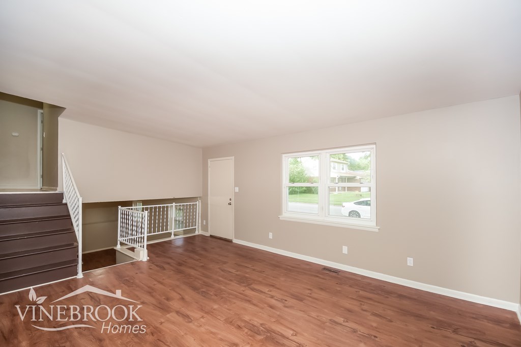 A room with a staircase and a window with a view of a house and trees outside.