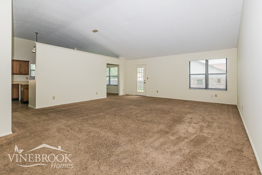 A spacious room with carpeted floor and white walls, with a logo of Vinebrook Homes in the bottom left corner.