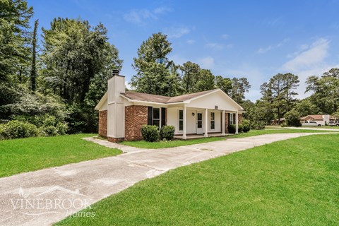 A house with a brick chimney is surrounded by greenery.