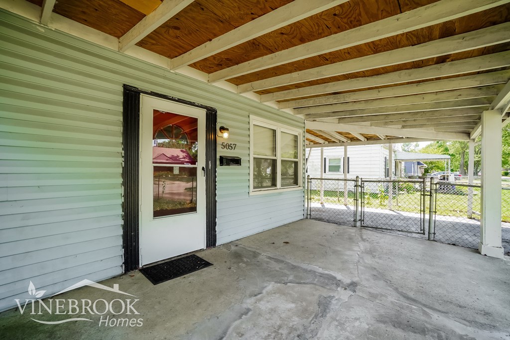 the covered front porch of a green house with a white door