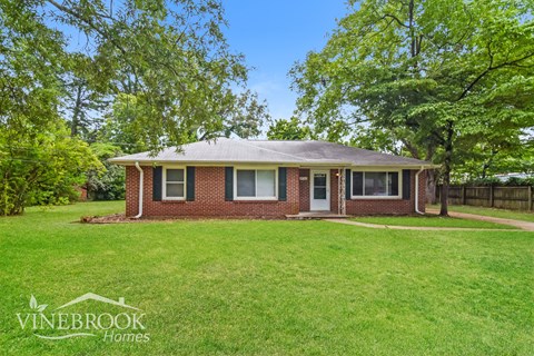 a small brick house with a green lawn and trees