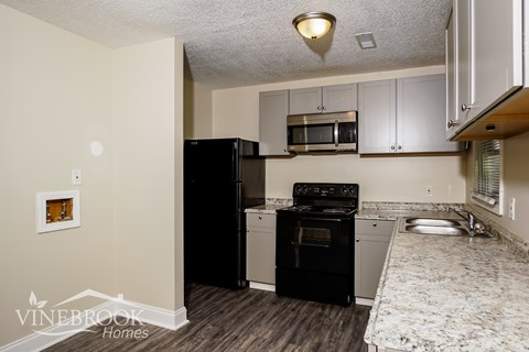 A kitchen with a black refrigerator and a sink with a granite countertop.