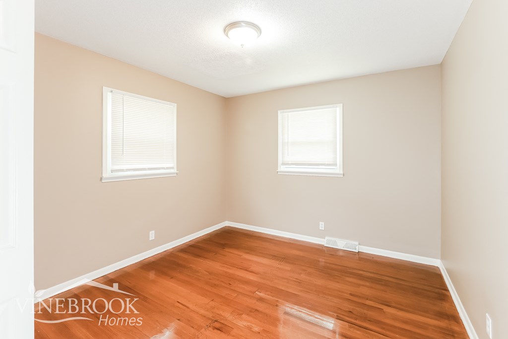a bedroom with a hard wood floor and two windows
