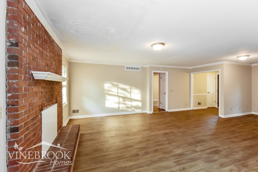 an empty living room with a brick fireplace and wooden floors