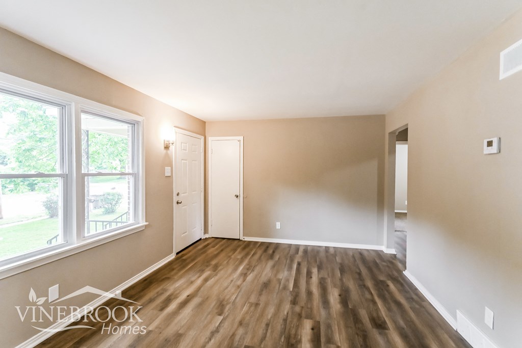 the living room of an empty house with wood flooring and a large window