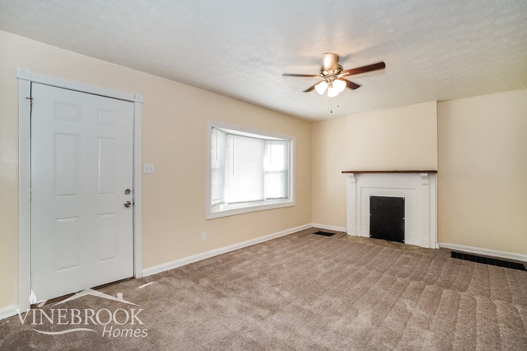 an empty living room with a fireplace and a ceiling fan