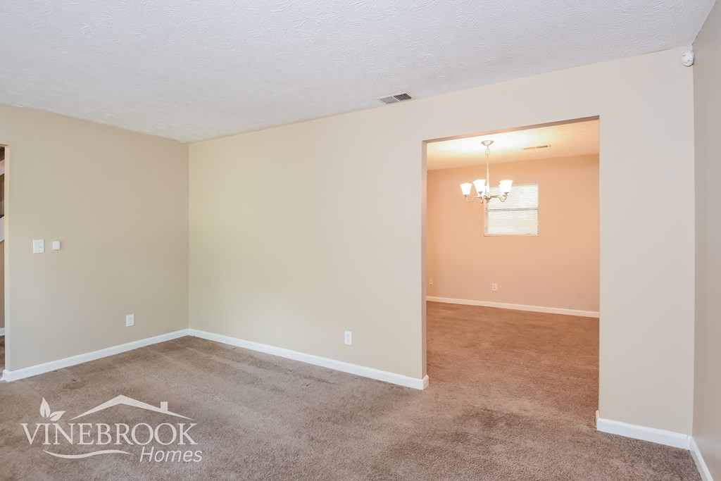 the living room and dining room with carpeting and a chandelier