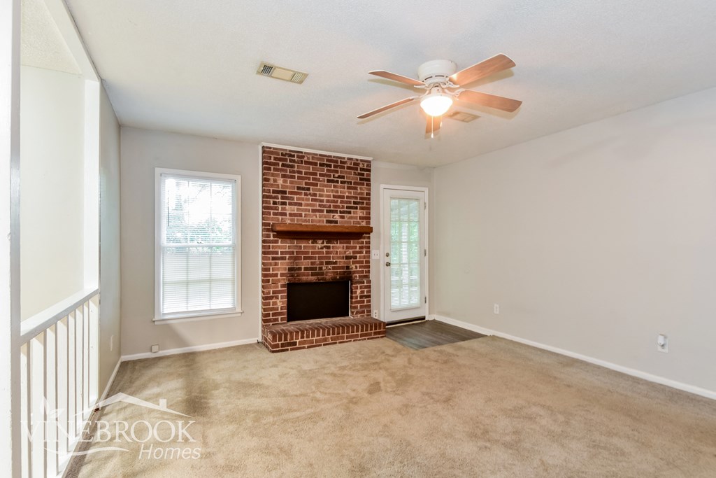 an empty living room with a brick fireplace and a ceiling fan