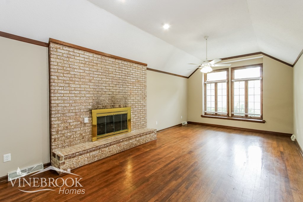 an empty living room with a brick fireplace and wood floors