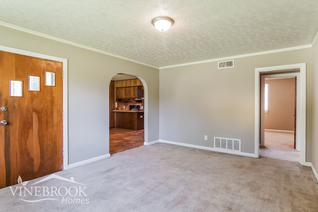 an empty living room with a door to a kitchen