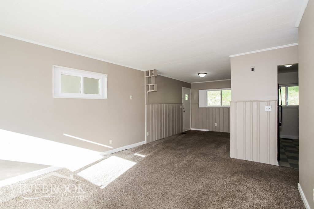 an empty living room with carpet and a door to a kitchen