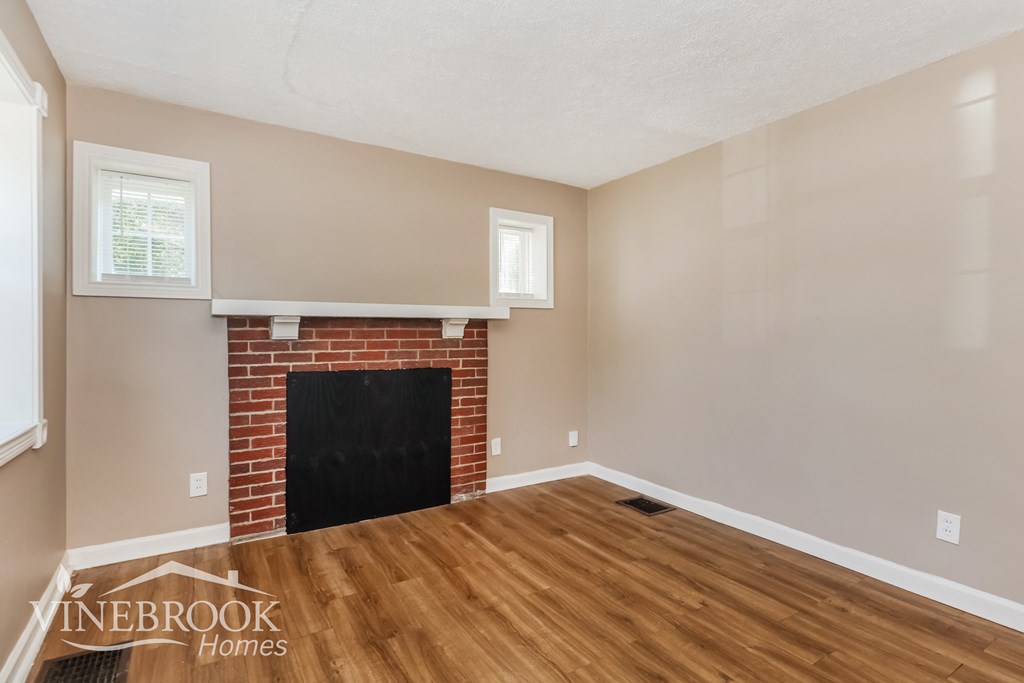 the living room of a home with wood flooring and a brick fireplace