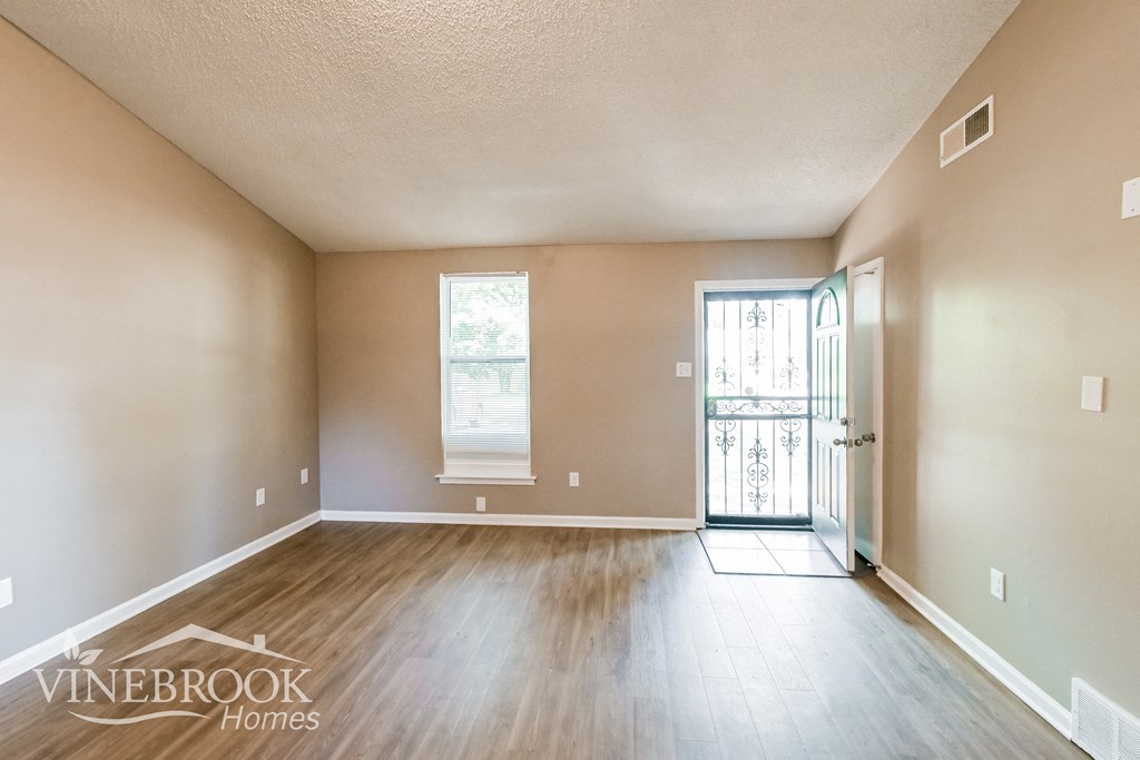an empty living room with wood floors and a door to a balcony