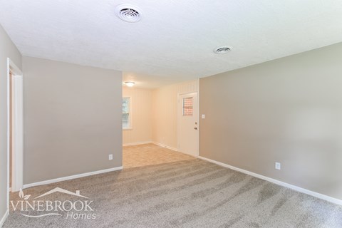 the living room and dining room of a home with carpeting and grey walls