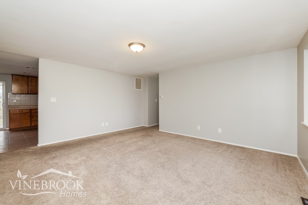 A spacious room with a carpeted floor and white walls, with a logo of Vinebrook Homes in the bottom left corner.