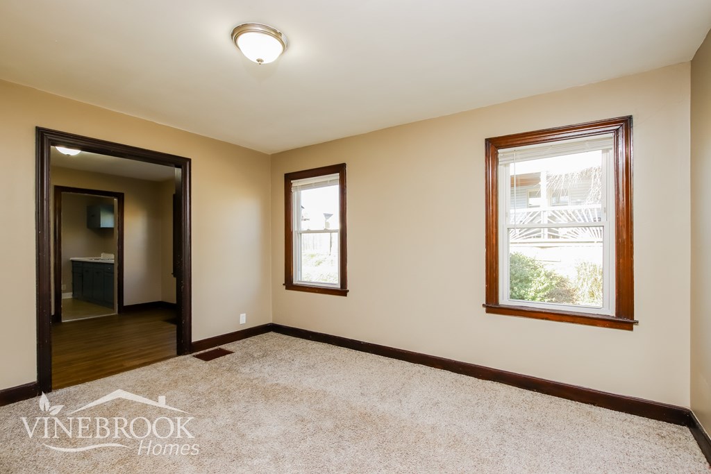 A room with a carpeted floor, a window, and a door leading to another room.