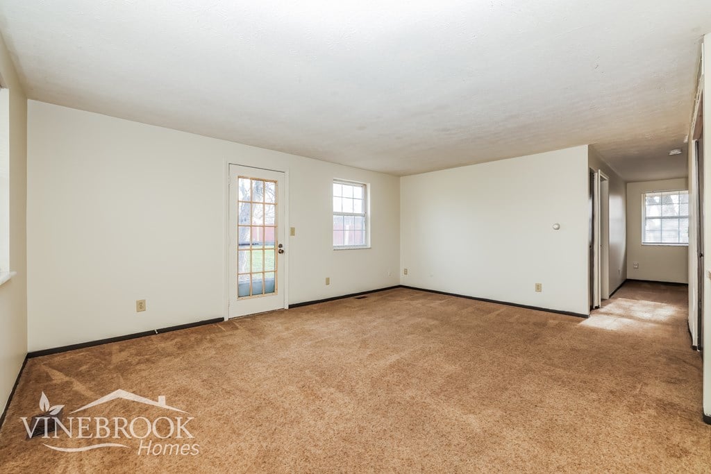 A room with carpeted floor and white walls, with a logo for Vinebrook Homes in the bottom left corner.