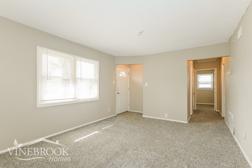 A spacious empty room with carpet flooring and two doors.