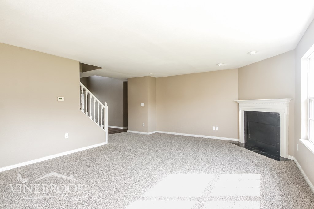 A spacious living room with a fireplace and a staircase.