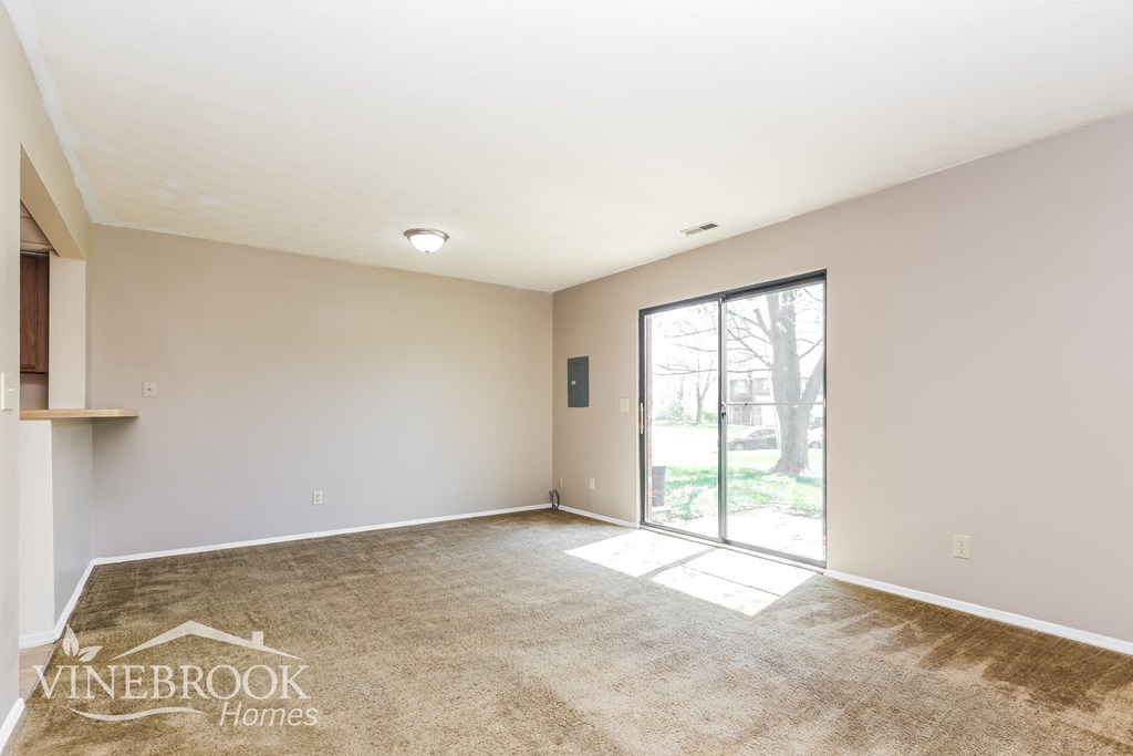 A spacious room with a carpeted floor and a sliding glass door leading to a balcony.