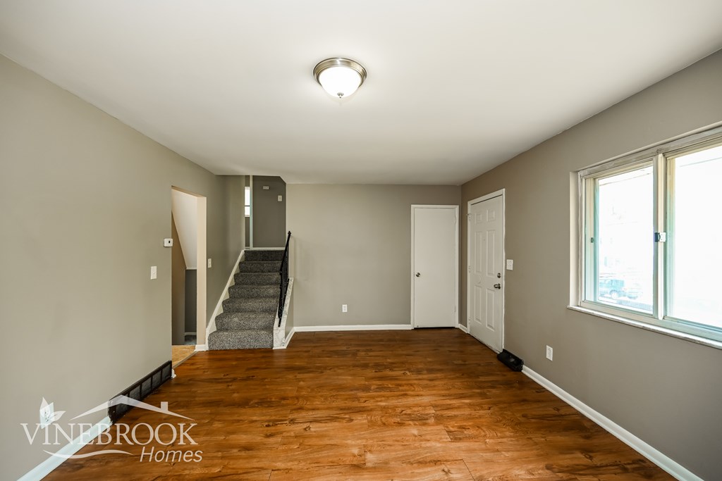 A room with wood flooring and a staircase leading to another room.