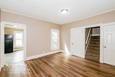 A room with wooden floors and a staircase leading to another room.