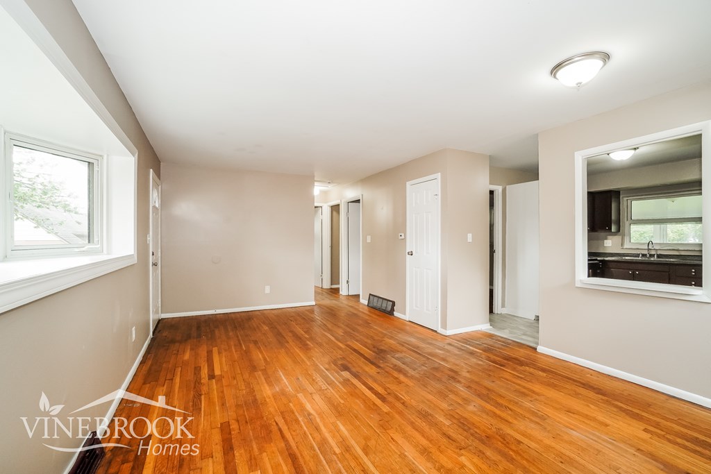 A room with wooden floors and white walls, with a window on the left and a door on the right.