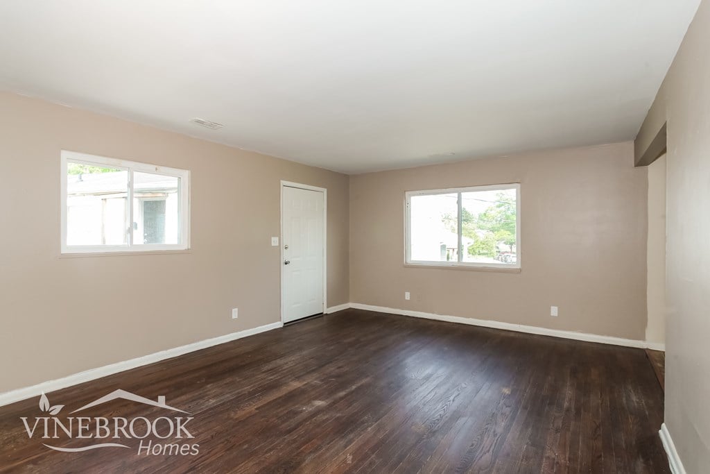 A room with wooden floors and two windows, one of which is open.