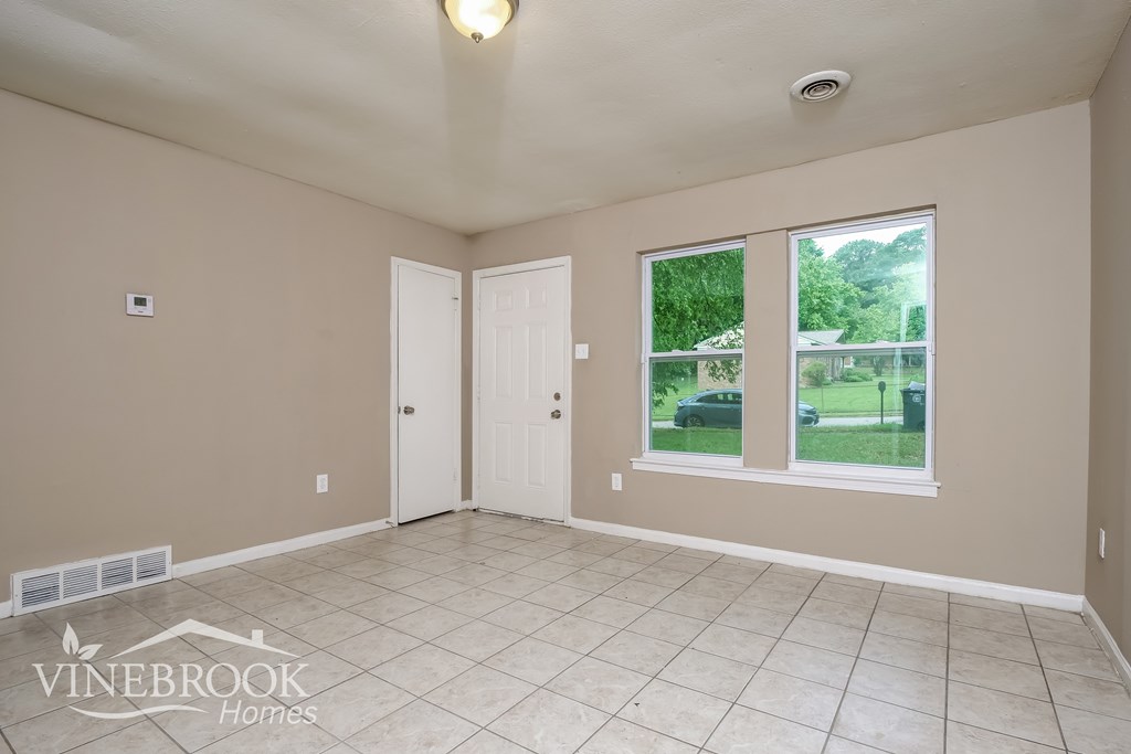 A room with a white door and a window with a view of a green area outside.