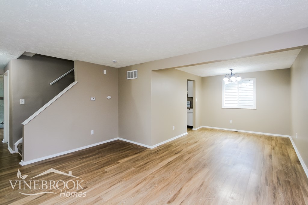 A spacious room with wooden flooring and a staircase on the left side.