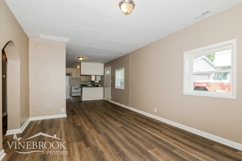 A room with wood flooring and a window showing a red building outside.