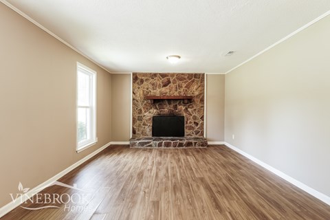 A large empty room with a stone fireplace and wooden floors.