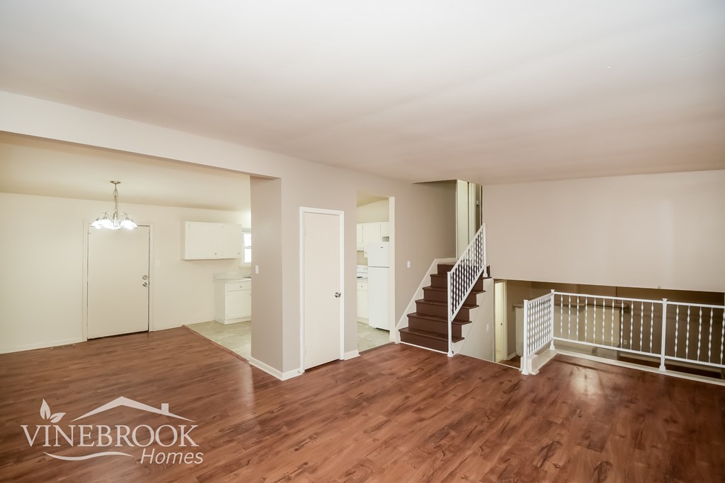 A spacious room with wooden floors and a staircase leading to another level.