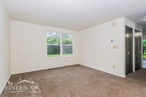 A room with a carpeted floor and a window with a view of trees outside.
