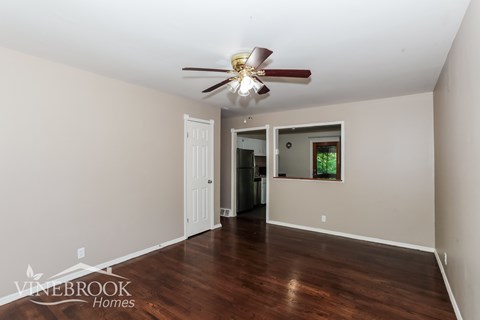 A room with a ceiling fan and a door leading to a kitchen.