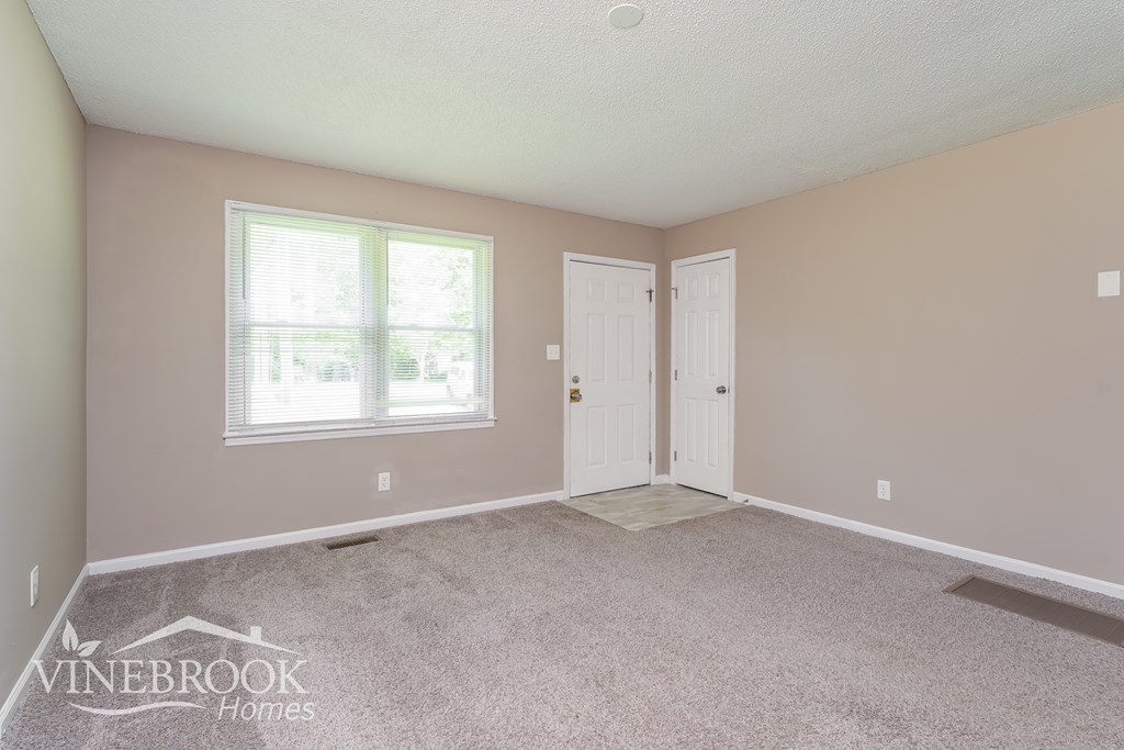 A room with a carpeted floor, two doors, and a window with blinds.