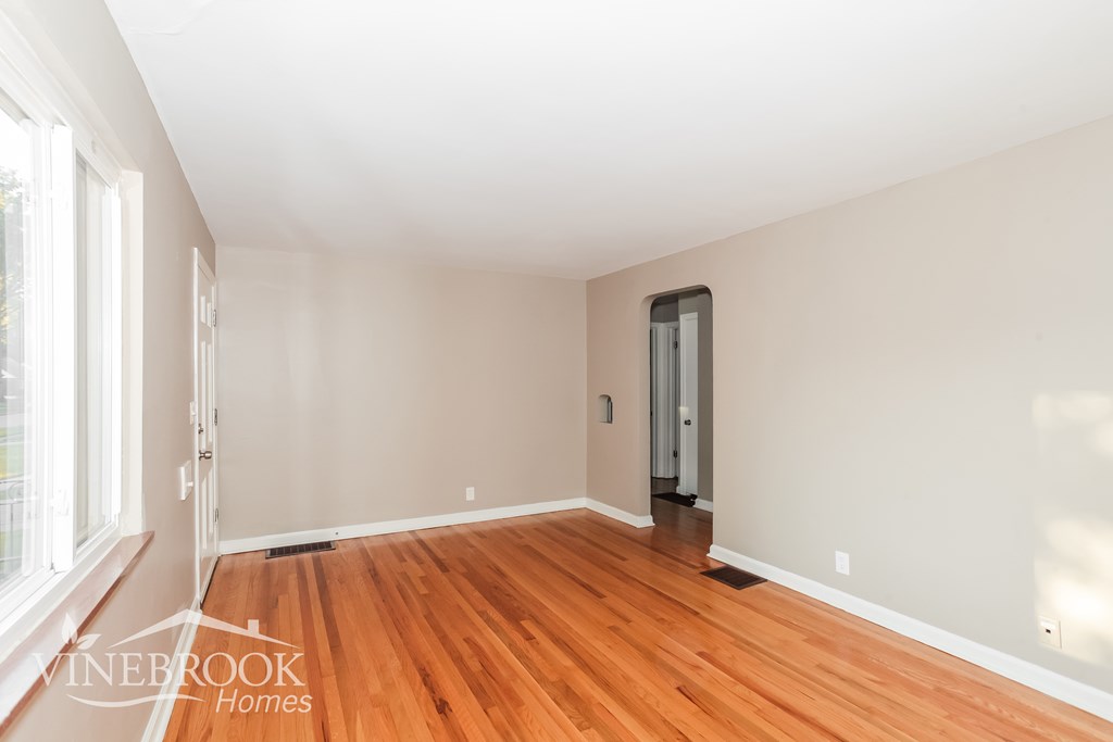 A room with wooden floors and white walls, with a door and a window.
