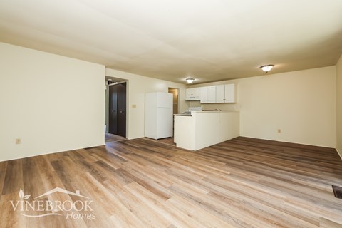 A room with wood flooring and a kitchenette in the corner.