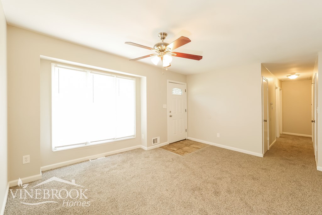 A room with a carpeted floor and a ceiling fan.