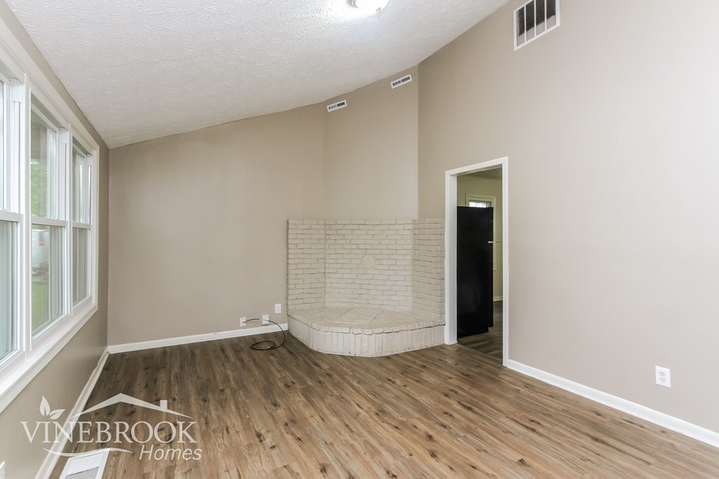 A room with wooden flooring and a brick wall in the corner.