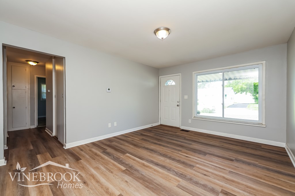 A room with wood flooring and a window with a view of trees.