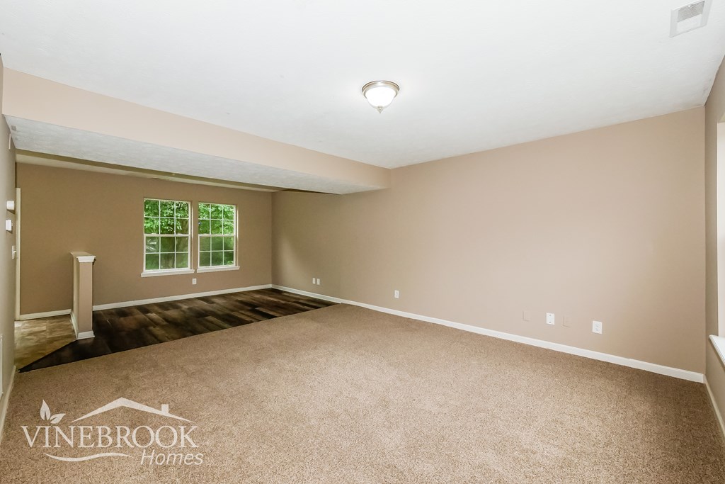 A room with beige walls and carpet flooring, with a window and a pillar in the corner.