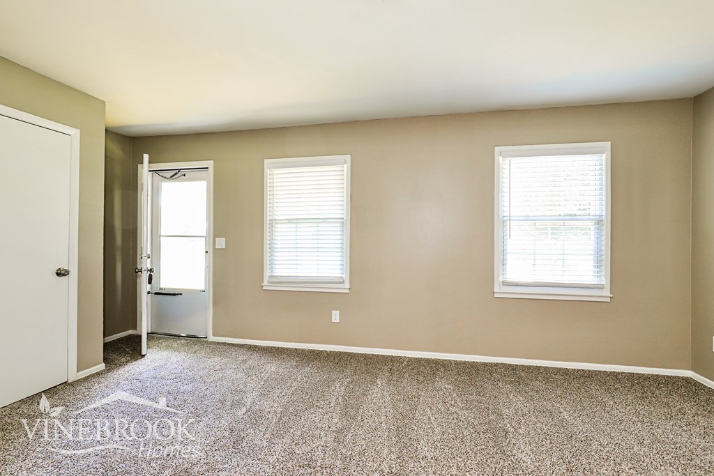 A room with a carpeted floor and two windows.