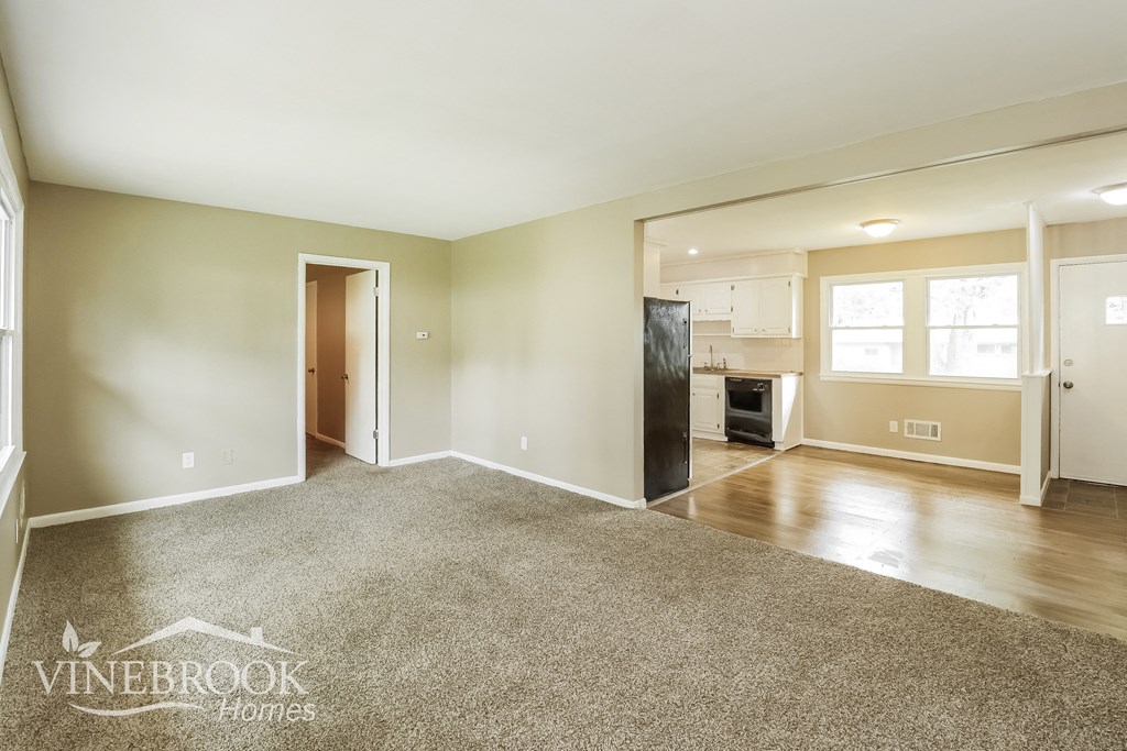 an empty living room with a kitchen in the background