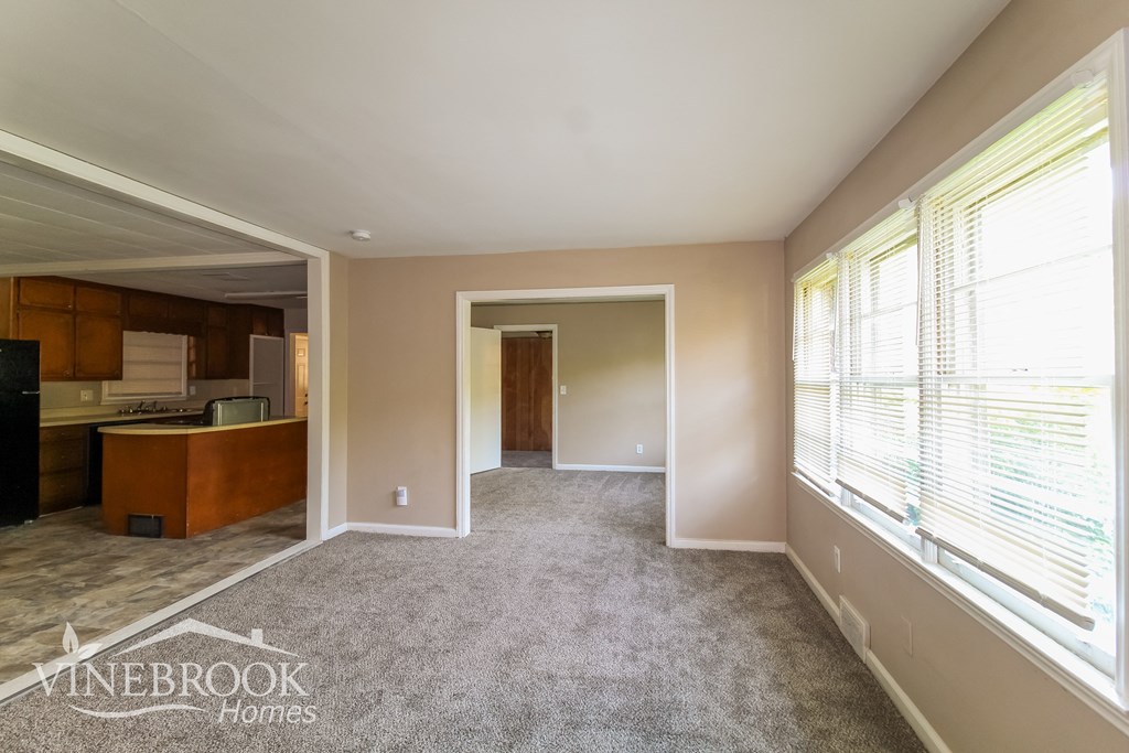 a carpeted living room with a large window and a kitchen