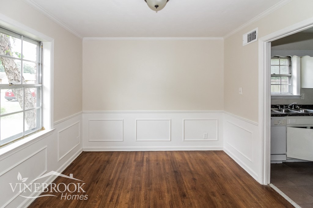 A room with wood floors and white walls, with a window on the left and a doorway on the right.