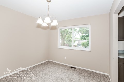 A room with a carpet floor, a chandelier, and a window showing trees outside.