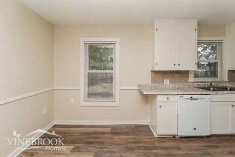 A kitchen with white cabinets and a window with blinds.