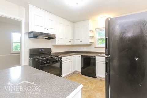 A kitchen with a black refrigerator and white cabinets.
