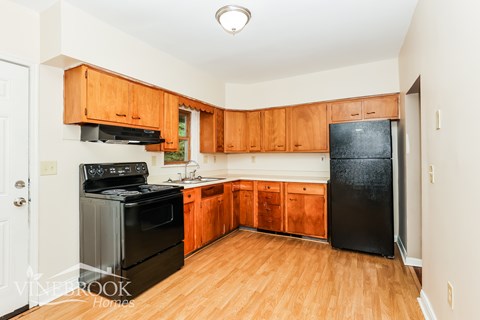 A kitchen with wooden cabinets and a black fridge.